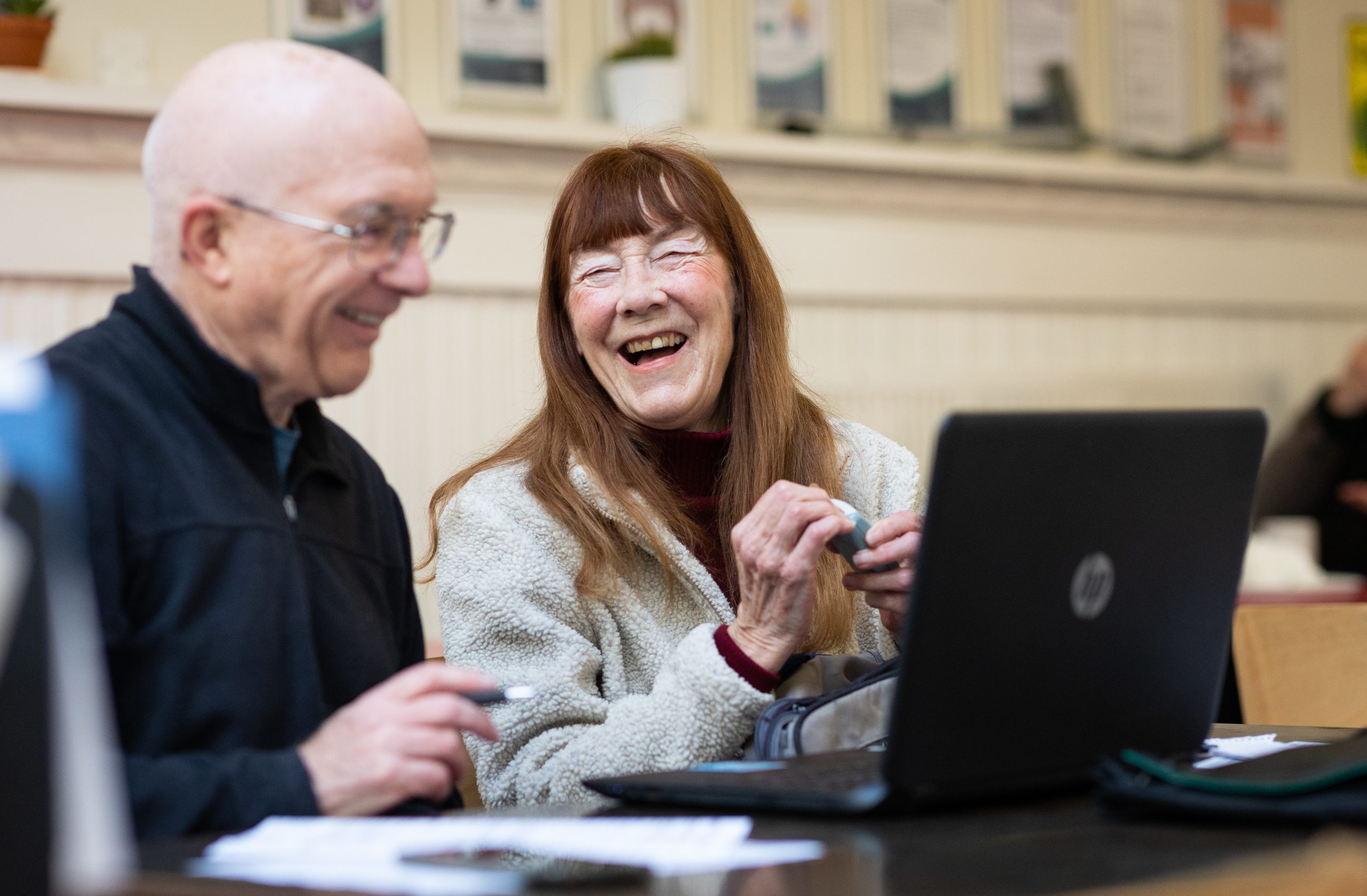 Two older people smiling and using a laptop.