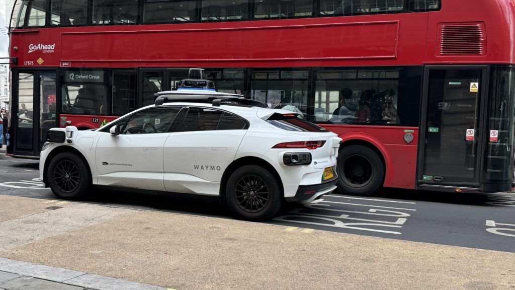 Waymo car in London, with a red bus behind it.
